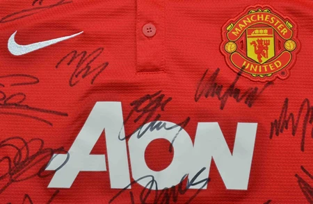 Close-up of a signed Manchester United red jersey featuring the AON logo and club crest.
