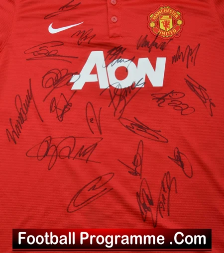 Red Manchester United jersey covered in signatures, with the AON sponsor logo and Nike swoosh visible.