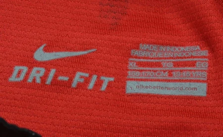 Red athletic fabric featuring the white Nike swoosh and 'DRI-FIT' logo; a care tag reads Made in Indonesia and shows size/production details.
