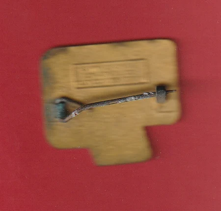 Blurry close-up of a small beige rectangular component with a curved metal rod across it, mounted by two screws on a red background.