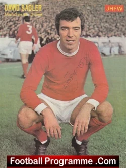 David Sadler kneeling on a football pitch in a red kit, autograph on chest; stadium crowd and another player in red in the background (Football Programme cover).