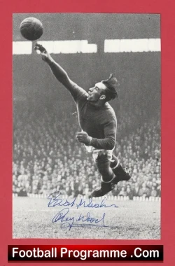 Black-and-white photo of a soccer goalkeeper leaping to catch a ball during a match, with a crowd behind and a red border reading Football Programme.com مستبد