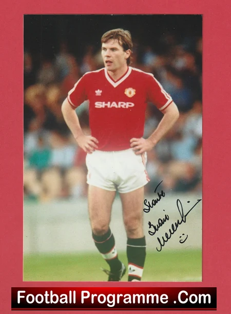 Male footballer in a red Manchester United kit standing with hands on hips on the pitch; autograph signature on the photo.