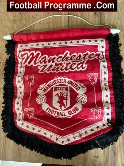 Red Manchester United football club pennant with crest and fringe, hanging on a wooden surface