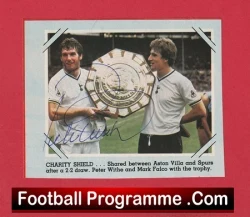 Two soccer players in white shirts hold a large Charity Shield trophy on a red football programme cover.