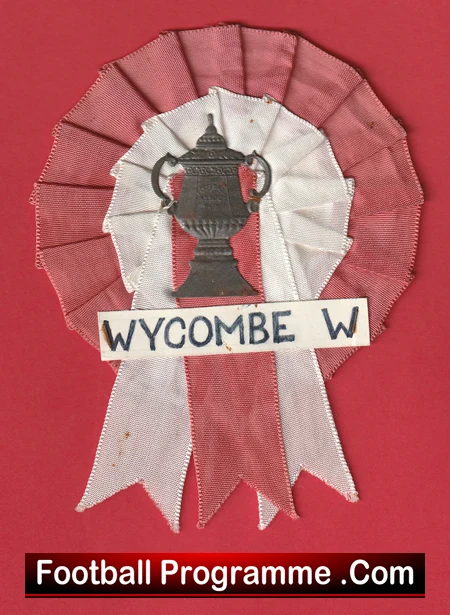 Red and white rosette award with a central trophy image and a label reading 'WYCOMBE W' on a white band, set on a red background.