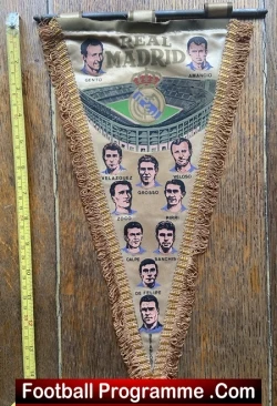 Real Madrid pennant with crest and small player portraits along the edges, hung on a wooden surface with fringe.