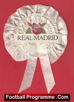 Cream satin rosette badge featuring the Real Madrid emblem and the text REAL MADRID, with two hanging ribbons, set against a red background (bottom banner reads Football Programme .Com).